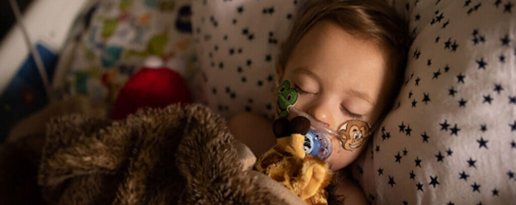 Young girl in hospital bed with oxygen tube cuddling a giraffe teddy