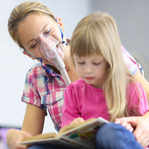 An adult female with oxygen support in a wheelchair with a child sat on her lap while reading
