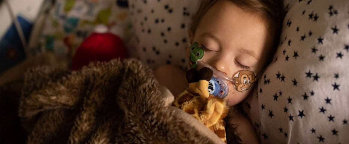 Young girl in hospital bed with oxygen tube cuddling a giraffe teddy