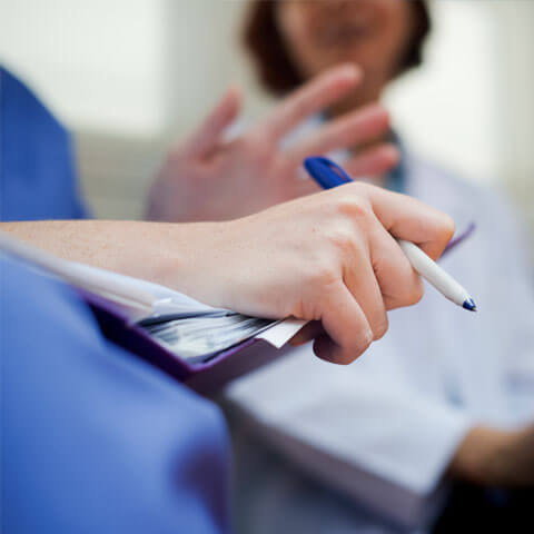 Health care worker with a clipboard and pen talking with other healthcare professionals