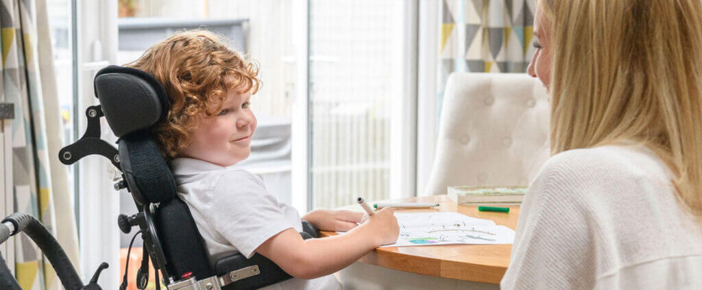 Boy in wheelchair at a table writing and smiling
